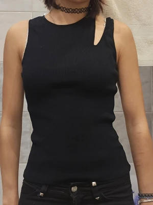 Svart ribbad ärmlös topp - ❗️Skriv innan köp❗️Svart ribbad topp med cut-out detalj vid axeln. Toppen är ärmlös och har en tight passform som framhäver figuren. Har fått secondhand, lite svår att få på om man har bredare axlar.