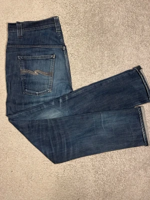 Mörkblå Nudie Jeans  - Säljer ett par mörkblå jeans från Nudie med en tvärsnygg tvätt i modellen Tape Ted i storleken 33/32. Jeansen är väl omhändertagna och har inga som helst skavanker på utsidan. Däremot har jeansen ett hål i höger framficka men går enkelt att laga. Skriv ifall du har några frågor🙋