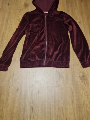 Vinröd velourhoodie med dragkedja - Mysig hoodie som är mjuk med dragkedja framtill och ficka. Hoodien har långa ärmar, ribbade muddar och en klassisk huva. Perfekt för dig som gillar en chill och stilren look.