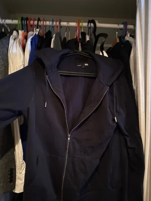 Mörkblå hoodie med dragkedja - Snygg mörkblå hoodie från H&M med dragkedja framtill och justerbar huva med snören. Klassisk modell med fickor på sidorna och mjukt material som känns skönt mot huden. Perfekt för en avslappnad och stilren look.