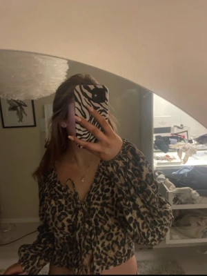 Leopardmönstrad blus med knytning - Trendig blus med leopardmönster och v-ringning med knytband framtill. Blusen har långa ärmar och är tillverkad i ett lätt och flödande material som ger en cool och avslappnad look. Perfekt för att skapa en statement outfit. Använd 2 gånger