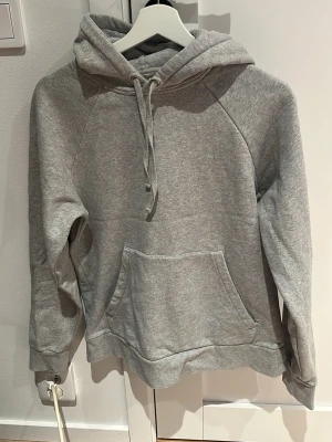 A day’s march hoodie - En klassisk grå hoodie med huva och dragsko, samt en stor magficka framtill. Tröjan har långa ärmar och ribbade muddar vid ärmslut och nederkant. Perfekt för en avslappnad och stilren look.litet litet hål vid snöret