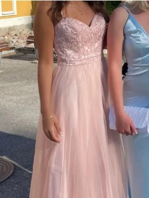 Ljusrosa långklänning med spetsliv -  ljusrosa balklänning med spetsliv och v-ringad urringning. Kjolen är i flera lager tunn tyll. Axelbandsmodell och figurnära passform upptill. Lägger ut den billigt (köpte den för 1700), eftersom den ej är kemtvättad och lite smutsig - den som köper kan då stå för kemtvätt. Pris kan diskuteras. På sista bilden ser ni ett sidenband som ni får med.