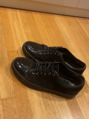 Svarta lanvins - Snygga svarta sneakers med rund tå och snörning. Skorna har en mix av material med både mocka och skinn, vilket ger en stilren look. Passar perfekt till jeans eller casual outfits.