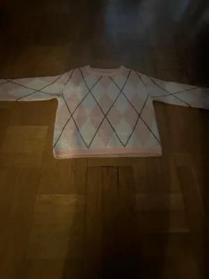 Pastellfärgad argyle stickad tröja - Säljer en söt stickad tröja i pastellrosa och vitt med klassiskt argylemönster. Tröjan har långa ärmar, rund halsringning och ribbade muddar. Perfekt för dig som gillar en mjuka plagg. Storlek xs