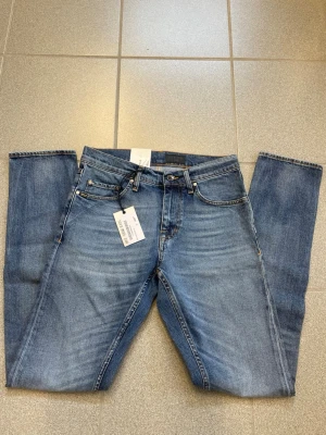 Blå jeans  Tiger of Sweden - Säljer ett par klassiska blå jeans från Tiger of Sweden. Jeansen har rak passform, fem fickor och snygga slitningar framtill. Tillverkade i denim med en tidlös look och normal midja. Perfekta till vardagsstilen!