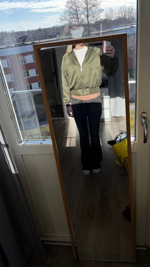 Olivgrön bomberjacka med dragkedja - Snygg olivgrön bomberjacka med klassisk ribbad mudd i midja och ärmslut. Jackan har dragkedja framtill och en avslappnad passform. Perfekt för dig som vill ha en trendig och enkel look. Passar till jeans och sneakers.