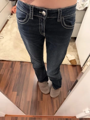 Mörkblå bootcut jeans med brodyr - Säljer ett par mörkblå bootcut jeans med kontrastsömmar och snygg broderad bakficka med paljettdetaljer i guld och silver. Jeansen är midwaist/ låg midjade.💖💖