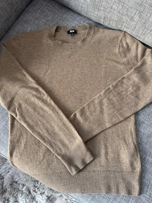 Beige cashmere tröja från Uniqlo - Mjuk och stilren beige stickad tröja från Uniqlo i 100% cashmere. Klassisk rund halsringning och långa ärmar med ribbade muddar. Enkel att matcha med allt. Mycket bra skick. Storlek xs. Passar ca 165-170 cm lång kille.