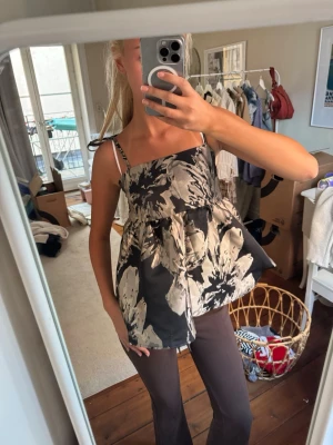 Blommig svart och silvrig linnetopp - Säljer en flowy linnetopp med svart botten och stora skimrande blommor. Toppen har tunna axelband som knyts på axlarna och en luftig, A-linjeformad passform. Perfekt till fest och enkel att styla med jeans eller kjol🩷