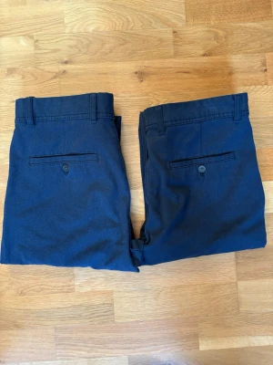Zara Melange Byxor - 2 par!! strl. 38 - Snygga mörkblå kostymbyxor med raka ben och klassisk passform. Byxorna har två bakfickor med knapp och hällor för bälte. Perfekta för en stilren look. Materialet ser ut att vara bomull eller en bomullsblandning.