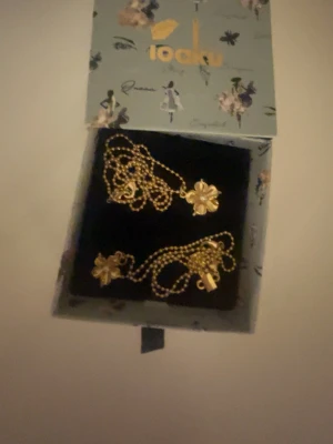 Guldigt halsband med blomma från Ioaku - De två halsbanden var köpta tillsammans som produkt men vill du köpa en enskild är det bara att skriva 💓💓Snyggt halsband i guldton från Ioaku med två lager och blommiga hängen. Kedjan har små kulor och blommorna är detaljerade och glänsande. Perfekt accessoar för att lyfta din outfit med en elegant touch.