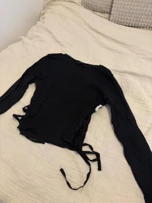 Svart långärmad topp med snörning - Säljer en svart långärmad topp med snörning i sidorna. Toppen har en tight passform och är tillverkad i ett mjukt material som känns skönt mot huden. Perfekt för dig som gillar trendiga detaljer och vill ha något som sticker ut. Kontakta mig vid intresse eller vid egna bud