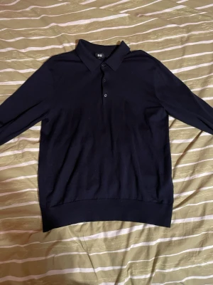 Mörkblå pikétröja från Uniqlo - Snygg mörkblå långärmad pikétröja från Uniqlo med klassisk krage och knäppning framtill. Tillverkad i mjukt material som känns skönt mot huden. Perfekt för dig som gillar stilrena och enkla plagg. Väldigt enkel att styla! Använd endast ett par gånger. Storleken är M. Priset ligger på 150kr. Hojta till om du har frågor eller vill få fler bilder!