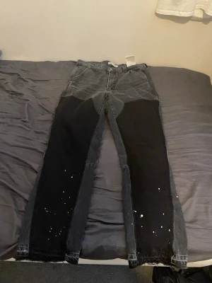 Svarta flared jeans från Zara - Unika svarta jeans med stora svarta patchar på framsidan och vita färgstänk på benen. Jeansen har en rak passform och cool kontrast mellan olika svarta nyanser. Perfekta för dig som gillar streetwear och vill sticka ut med din stil.