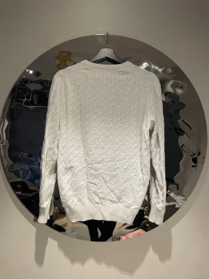 Vit kabelstickad tröja från East west - Säljer en vit kabelstickad tröja från East west med rund hals och ribbade muddar. Tröjan har ett klassiskt mönster och är tillverkad i mjukt material som passar perfekt för lager-på-lager. Långärmad och stilren design.