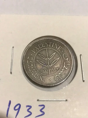Palestina mynt 1933 - Unikt mynt från Palestina, präglat 1933. Myntet är i silverfärg och har ett motiv med olivkvist samt text på engelska, arabiska och hebreiska. Perfekt för samlare av historiska mynt eller dig som gillar numismatik.