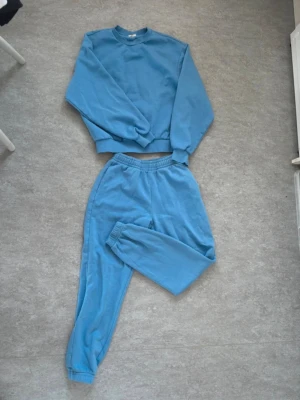 Gina Tricot, Tvådelat mjukisset XS/S - Ett matchande set i en fin blå färg från Gina Tricot ("basically basics"). Setet består av en sweatshirt i storlek S och ett par mjukisbyxor med mudd nedtill i storlek XS.  I fint använt skick! 