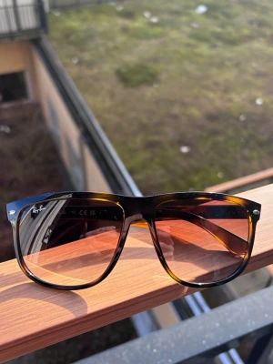 Bruna solglasögon från Ray-Ban - Snygga solglasögon från Ray-Ban med klassisk wayfarer-form. Bågarna har en brunskiftande sköldpaddsmönstrad look och glasen är tonade i brunt. Perfekta för soliga dagar och ger en cool vibe till din outfit.