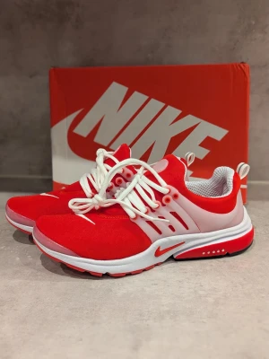 Nike Presto röda och vita sneakers - Snygga röda och vita Nike sneakers med vit sula och röda detaljer. Ovandelen är i mesh-tyg för bra andningsförmåga och har vita plastdetaljer vid snörningen. Klassisk Nike-logga på sidan och tungan. Perfekta för dig som vill sticka ut.