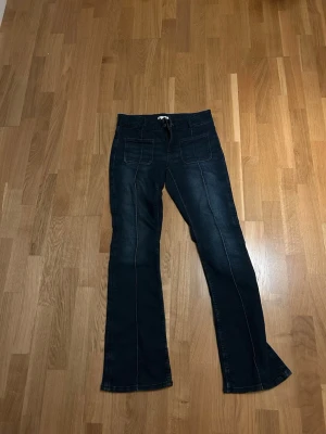 Mörkblå bootcut jeans med kontrastsömmar - Snygga mörkblå bootcut jeans med tydliga kontrastsömmar och framfickor. Jeansen har utsvängda ben och klassisk femficksdesign. Perfekta för dig som gillar en retroinspirerad look och vill ha ett par jeans som sticker ut lite extra.