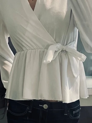 Vit omlottblus med knytband - Snygg vit omlottblus med knytband i midjan och v-ringning. Går att matcha till allting. Jättefint skick! 🤎
