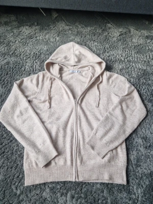 Zip hoodie - Mysig beige hoodie från Ryvls med dragkedja framtill och justerbar huva med snören. Tillverkad i mjukt stickat material som känns skönt mot huden. Perfekt för chill dagar eller när du vill ha en enkel och clean look. Det står att tröjan passar om man är 158-164 cm lång. Men tröjan är väldigt stretchig. Jag är 174 och tröjan är lite liten för mig, därför skulle jag säga att den sitter som en XS (Man storlek)