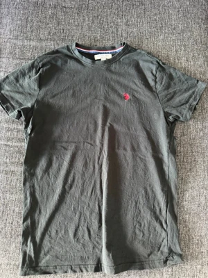 Svart t-shirt från Polo Ralph Lauren - Klassisk svart t-shirt från Polo Ralph Lauren med röd broderad logga på bröstet. T-shirten har rund halsringning och korta ärmar. Tillverkad i mjuk bomull för en skön känsla och enkel stil.