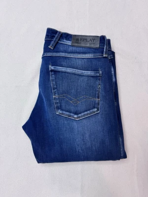 Blå jeans från Replay, dżinsy - Snygga blå slim fit jeans från Replay med klassisk femficksmodell och ljusa slitningar på låren. Jeansen har en bakficka med dekorativ söm och Replay-logga på linningen. Tillverkade i mjukt denimtyg som ger en skön passform. Midjemått: 40cm byxlängd: 102 cm !!priset kan diskuteras!!