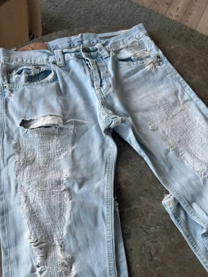 Dondup Jeans - Säljer ett par ljusblå jeans med rejält slitna detaljer och stora hål på både fram- och baksida. Jeansen har klassisk femficksmodell och är tillverkade i denim. Perfekta för dig som gillar en edgy och avslappnad stil.