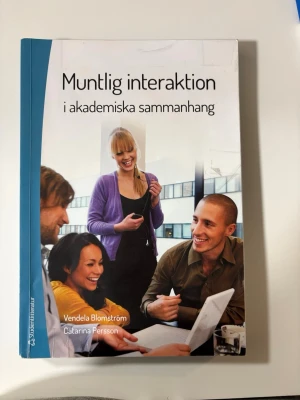 Muntlig interaktion i akademiska sammanhang - Kursbok med blå och vit framsida, titeln 'Muntlig interaktion i akademiska sammanhang' av Vendela Blomström och Catarina Persson. Boken riktar sig till universitetsstudenter och behandlar muntlig kommunikation i akademiska miljöer. Mjukt omslag, tryckt text och färgbilder på framsidan.