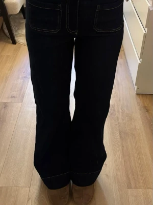 Mörkblå raka jeans med fickor - Säljer ett par mörkblå jeans med raka ben och stora bakfickor. Jeansen har kontrastsömmar och hög midja, vilket ger en snygg och tidlös look. Perfekta till sneakers eller boots för en avslappnad stil.