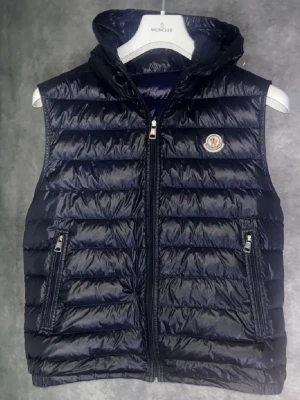 Moncler väst - Snygg mörkblå Moncler med luva. Storlek 3 men sitter som M. Små hål men inget som syns man ser de inte när man har på sig västen och ser de inte ens på bilderna. Bästa priset på plick en riktig steal🤑🤑Perfekt inför sommaren