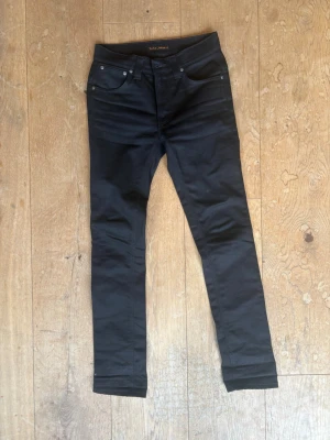 Svarta skinny jeans från Nudie Jeans - Säljer ett par svarta skinny jeans från Nudie Jeans med klassisk femficksmodell och låg midja. Jeansen har smal passform hela vägen ner och är tillverkade i stretchigt denimtyg för extra komfort. Perfekta för dig som gillar en clean och stilren look.