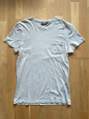 Bash t-shirt från Morris med ficka och brodyr - Säljer en bash t-shirt i bomull med korta ärmar. På bröstet finns en liten ficka med en mörkblå broderad Morris logga. Perfekt basplagg! Nypris: 400kr