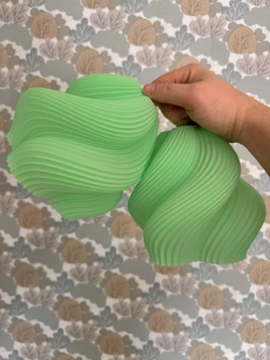 ÄppelGrön vågig lampskärm i plast 2 st - Säljer en unik, vågformad lampskärm i ljusgrön plast. Skärmen har ett modernt, skulpturalt utseende med mjuka, böljande linjer och passar perfekt för dig som vill ha en cool inredningsdetalj. Enkel att montera med E14 sockel. 