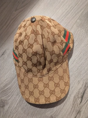 Beige keps - Säljer en beige keps. På sidorna finns gröna och röda ränder som ger en ikonisk touch. Kepsen har böjd skärm och är tillverkad i canvasmaterial.