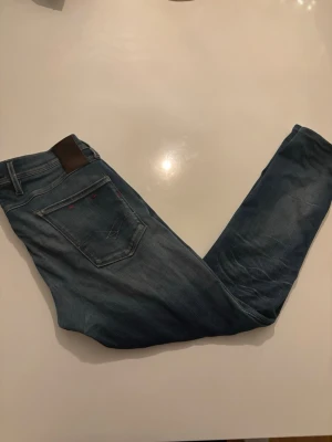 Blå jeans från Replay, midja 33/34 - Snygga blå jeans från Replay med klassisk femficksdesign och läderpatch bak i midjan. Jeansen har en rak passform och är tillverkade i bomull. Perfekta för dig som gillar en tidlös och avslappnad stil.