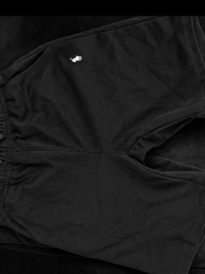 Svarta shorts från Polo Ralph Lauren - Svarta shorts från Polo Ralph Lauren med elastisk midja och liten vit logga broderad på vänster sida. Tillverkade i mjuk bomull som ger en skön och avslappnad känsla. Perfekta för sommardagar eller chill hemma.