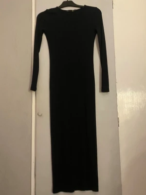Svart långärmad långklänning - En stilren svart långklänning med långärmar och rund halsringning. Klänningen har en slimmad passform och är enkel i designen, perfekt för dig som gillar minimalistiskt mode. Materialet känns mjukt och stretchigt, vilket gör den bekväm att bära.