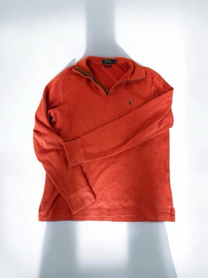 tröja från Polo Ralph Lauren - Säljer en orange långärmad tröja från Polo Ralph Lauren med klassisk broderad logga på bröstet. Tröjan har en half zip-dragkedja vid halsen och är tillverkad i mjukt bomullsmaterial. Perfekt för en avslappnad och stilren look.
