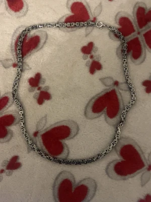 Kedjehalsband i silverfärg - Säljer ett stilrent halsband i silverfärgad metall med rektangulära länkar som ger en modern och edgy look. Halsbandet har ett klassiskt lås och passar perfekt för dig som vill ha en enkel men snygg accessoar till din outfit.