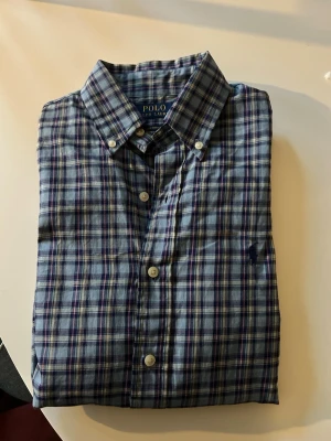 Rutig skjorta från Polo Ralph Lauren XS - Snygg rutig skjorta från Polo Ralph Lauren i blå och vita toner med inslag av lila. Skjortan har klassisk button-down krage, vita knappar och är i custom fit-modell. Perfekt för dig som gillar tidlös stil och vill ha något som funkar till många looks. Skicket är fint utan defekter. Storlek XS men passar S oxå skulle jag säga👍hör av er vid frågor✅ Skön för våren, valborg och sommarn😍