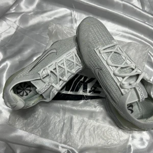 Nike Vapormax i vit - Snygga Nike Vapormax sneakers i vit färg med en futuristisk design. Skorna har en stickad ovandel och en genomskinlig sula med synliga luftkuddar för extra komfort. Perfekta för både träning och vardag. Luftbubblorna är trasiga 