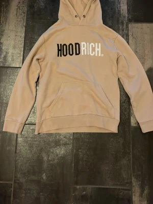 Beige hoodie från Hoodrich - Säljer en beige hoodie från Hoodrich med stor svart och vit logga på bröstet. Bra skick.
