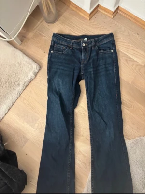 Mörkblå lågmidjade bootcut jeans - Snygga mörkblå jeans från Hm i strl 38. Jeansen har kontrastsömmar i orange. Materialet är mjukt denim i bomull.
