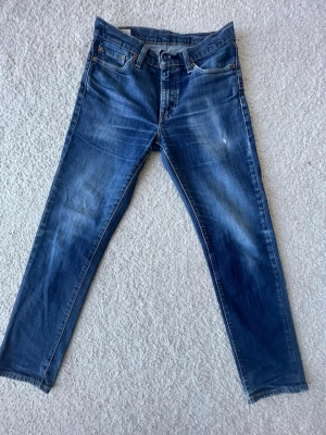 Blå faded Levi's jeans  - Snygga blå jeans från Levi's med klassisk femficksdesign och raka ben. Jeansen har en lätt tvättad look med subtila slitningar. Jeansen har lite slitningar under jeansen. Jeansen är i mycket bra skick då den inte har några defekter. Säljer för ett bra pris. 