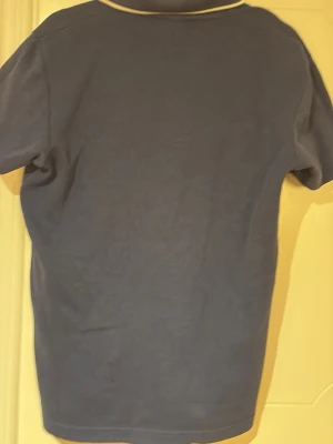 Blå t-shirt från Selected Homme - Snygg blå t-shirt från Selected Homme med vit kant runt kragen och v-ringning. Perfekt för en stilren och avslappnad look. Tillverkad i mjuk bomull som känns skön mot huden.