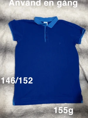 Blå pikétröja med krage - Klassisk blå pikétröja med ljusblå krage och knappslå. Tröjan har korta ärmar och en stilren look, perfekt till jeans eller shorts. skön känsla hela dagen.🌸 Använd en gång. Storlek 146/152