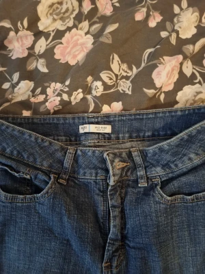 Bootcut jeans midwaist med broderade fickor - Snygga blå bootcut jeans från Riders i midwaist-modell. Jeansen har klassisk femficksdesign och coola broderade detaljer på bakfickorna. Materialet är 99% bomull och 1% elastan för skön stretch. Perfekt passform och stilren look. Köpta i butik för 499 kr!